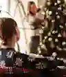 一个女人坐着看着她正在装饰圣诞树的女儿