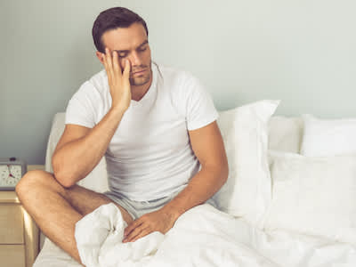 男人坐在床上，因为胃酸倒流而无法入睡。