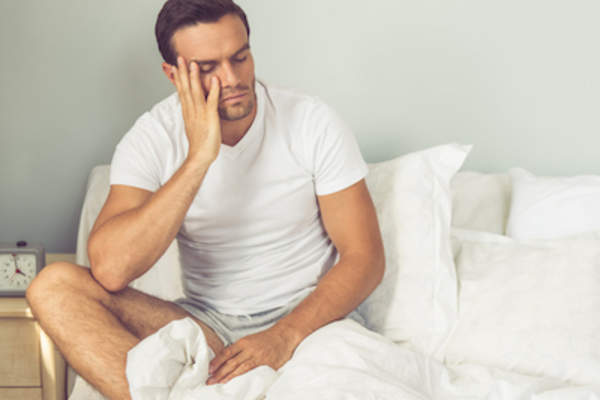 男人坐在床上,因为胃酸倒流而无法入睡。