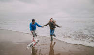 秋日，一对年轻夫妇带着小狗在海滩上玩耍。