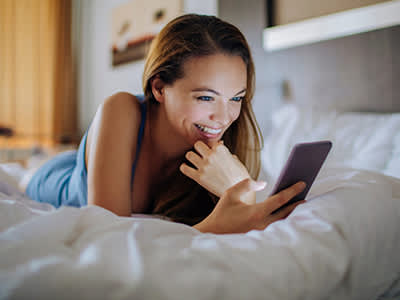 女子微笑着躺在床上，看着她的手机上的应用程序的生育。