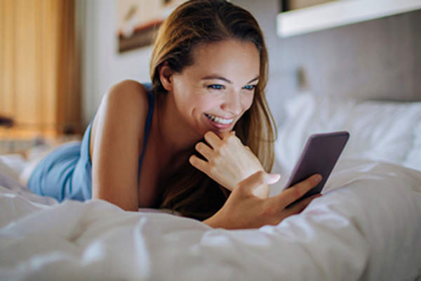 女子微笑着躺在床上,看着她的手机上的应用程序的生育。