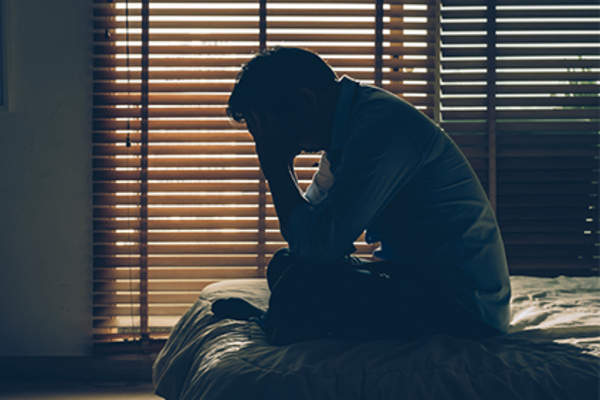 头痛的人坐在黑暗的房间的床上。