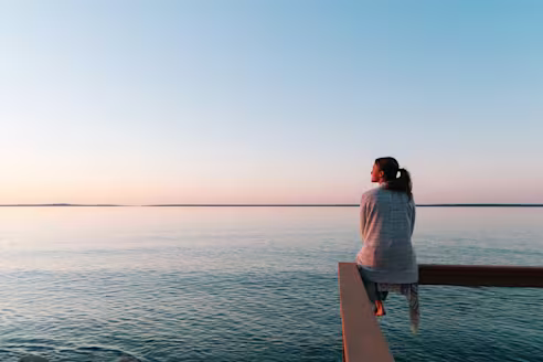 A woman sits on a ledge and looks at the ocean
