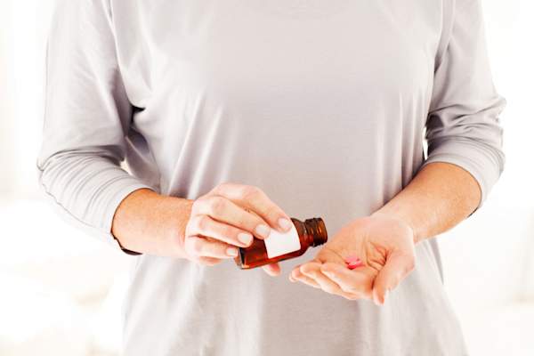 从瓶子里倒红色药丸的女人