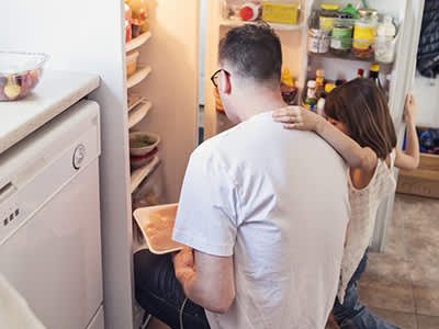 父亲抱着女儿从冰箱里拿食物。