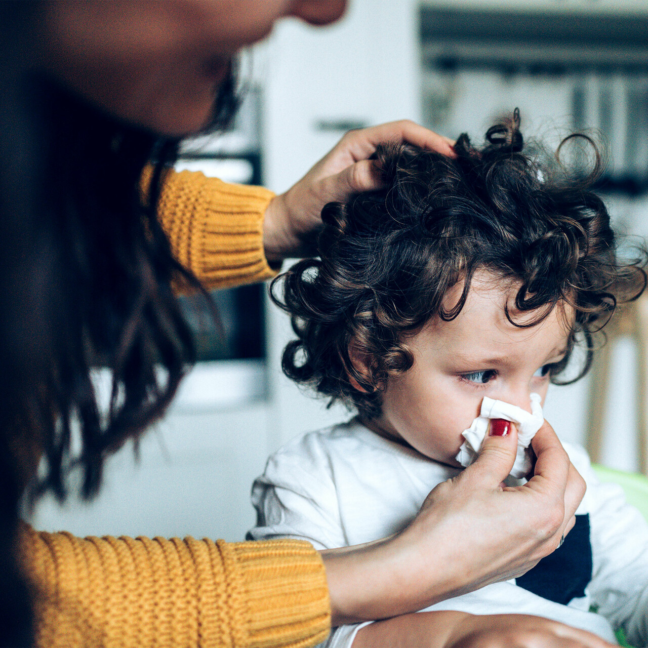 一个女人拿着一张纸巾放在一个男孩的鼻子上