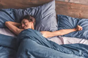 微笑的女人醒来后精神焕发，躺在床上伸展身体。