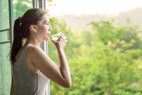 A woman drinks water by a window in the morning