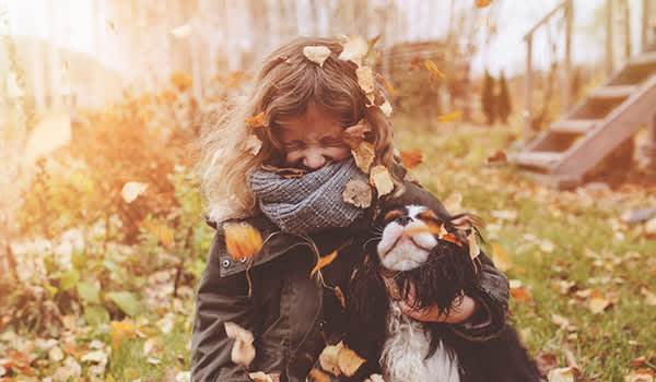 女孩和她的狗在秋叶中玩耍，脸上蒙着围巾。