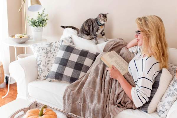 女人盖着毯子和猫在沙发上看书
