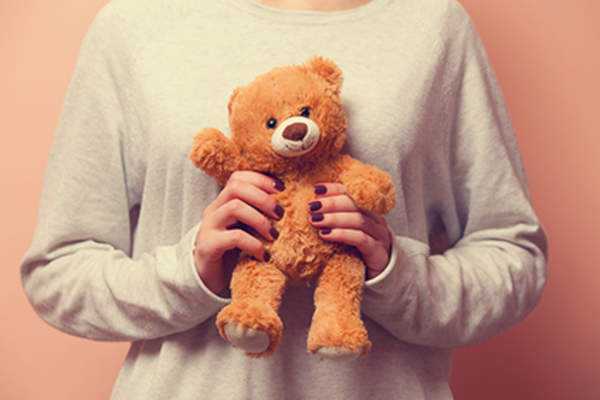 Woman cuddling a teddy bear for comfort.