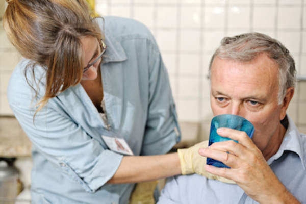 护士在男人喝水时检查他的喉咙。