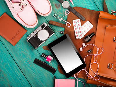 旅行袋溢出鞋，平板电脑，相机，化妆品，记事本，耳机，手表，丸剂，和护照。