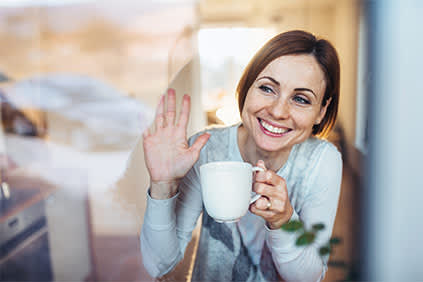 微笑的女人站在窗口，喝着咖啡说再见。