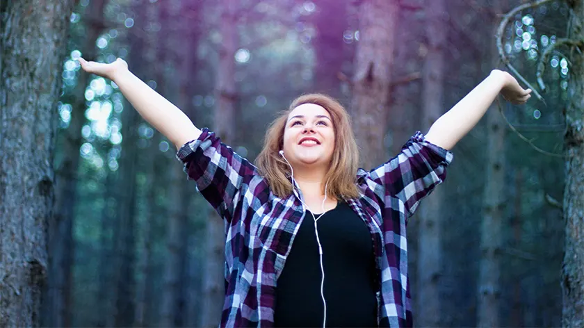 快乐的女人一边听着音乐一边在树林里散步。