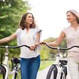 Smiling women friends walking bikes.