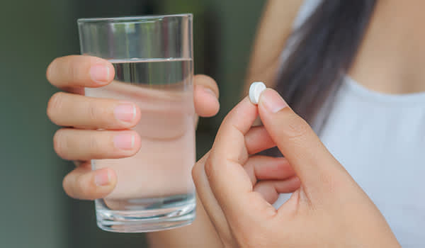 一个女人拿着一颗药丸和一杯水。