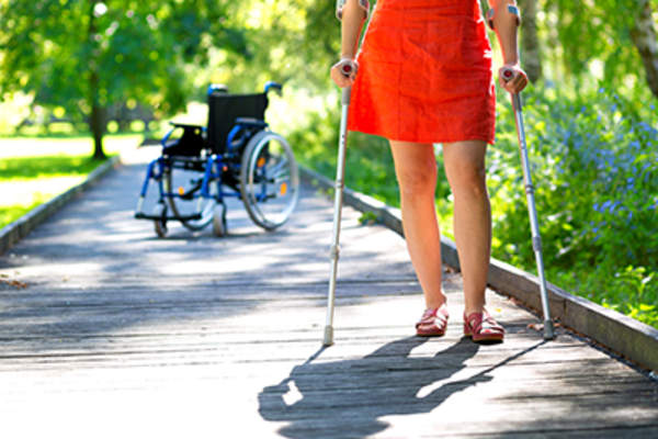 一名妇女拄着拐杖,背景是轮椅。