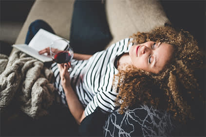 一个女人正在休息，一边看书一边喝着酒。