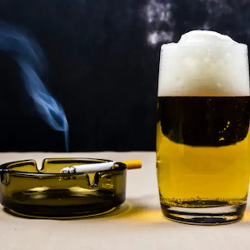 Cigarette in ashtray next to beer.