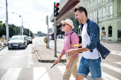 年轻人和盲人老人拄着白色拐杖在城市中行走，过马路