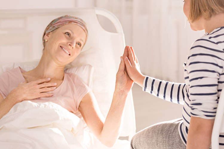 Mother with breast cancer smiling and touching her daughter's hand.