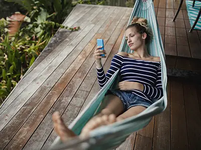 度假时拿着手机的年轻女子躺在吊床上休息。