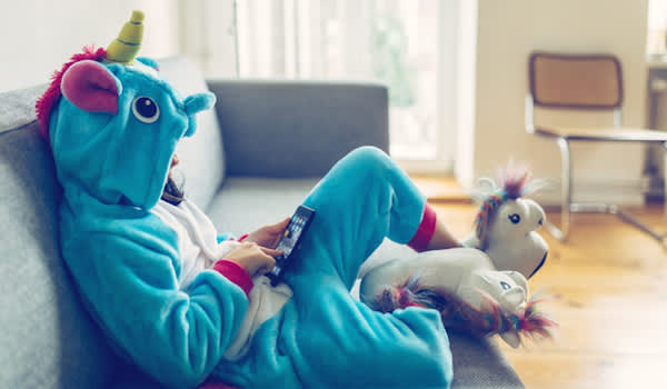 Child sitting on couch, in unicorn costume, quietly playing on phone.
