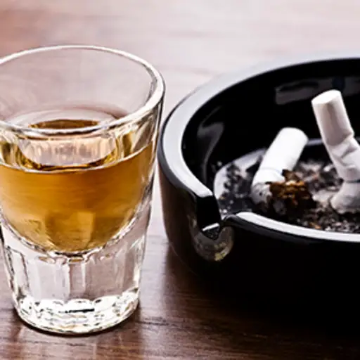 Alcohol next to cigarettes in an ashtray.
