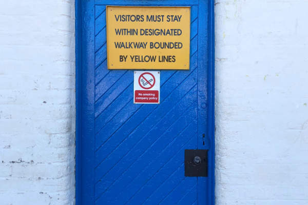 蓝色大门，上面写着“访客必须待在黄线环绕的指定通道内”