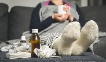 长沙发的病的妇女用茶，冷医学和被弄皱的Kleenex在奥斯曼托盘上。