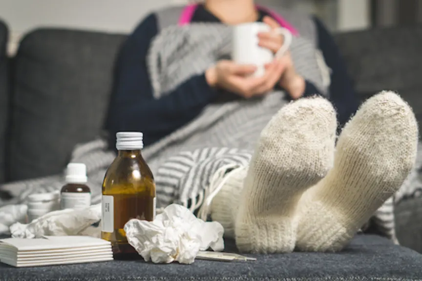 一个生病的女人躺在沙发上，喝着茶，吃着感冒药，还有揉皱的面巾纸躺在沙发上。