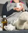 生病的女人躺在沙发上,喝茶,吃感冒药,皱皱的面巾纸放在沙发上。