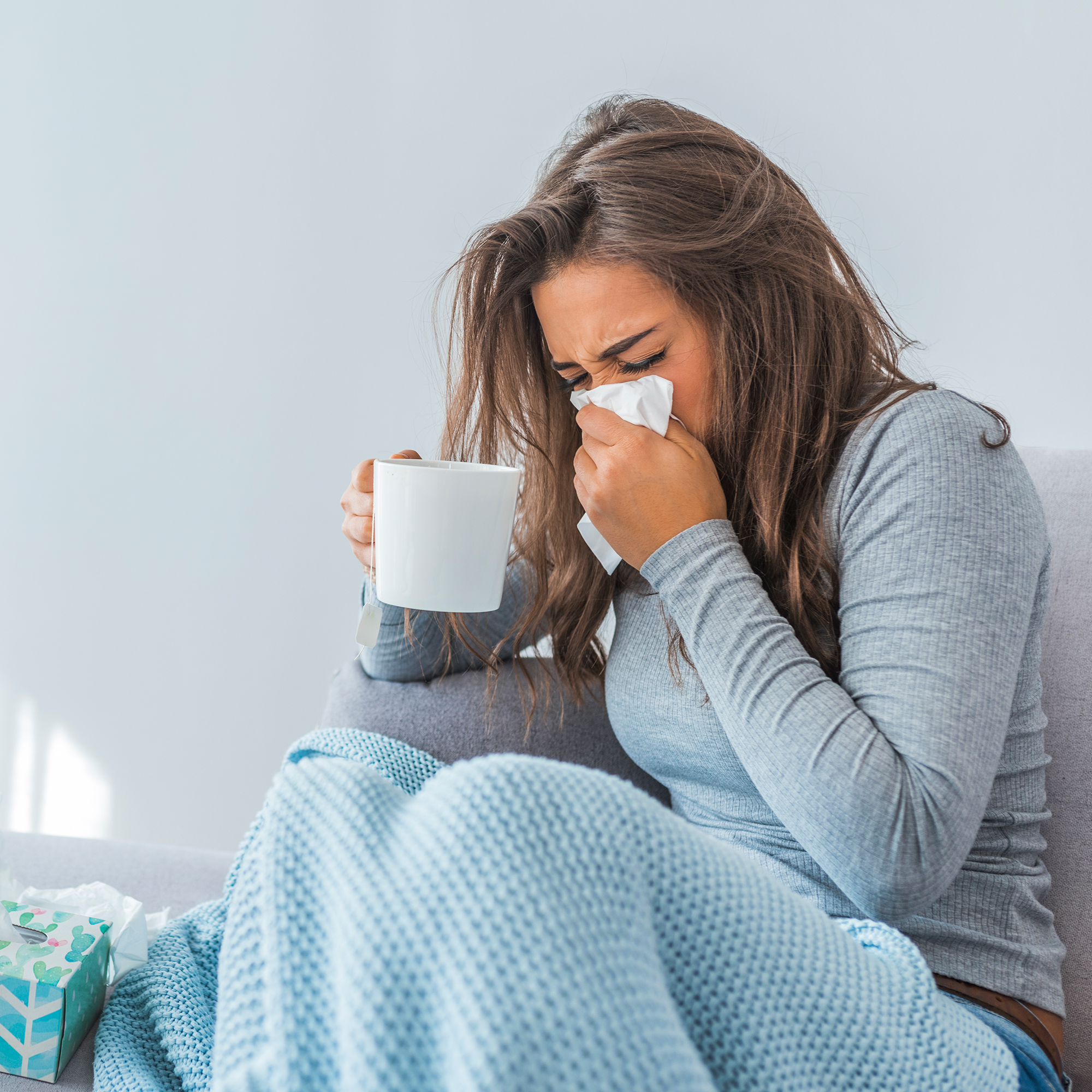 生病的女人一边喝茶一边擤鼻涕
