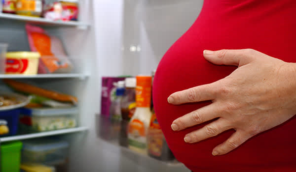 孕妇站在打开的冰箱前。