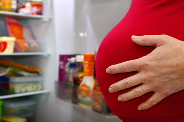 孕妇站在打开的冰箱前。