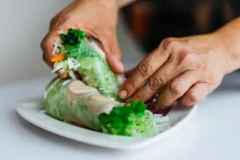 close up of hands picking up summer roll containing vegetables