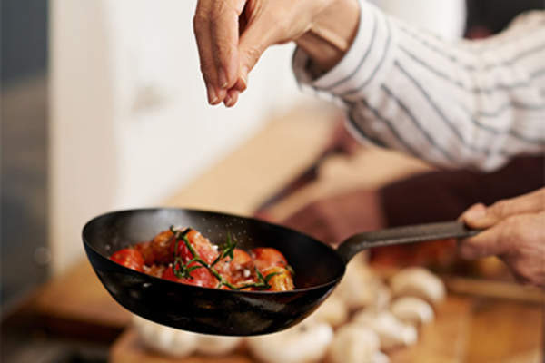 女人在煎锅里给食物加香料。