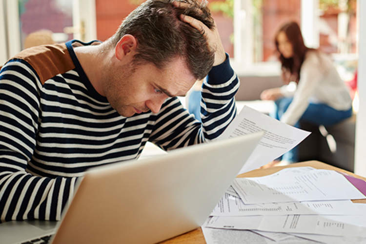 一个男人坐在笔记本电脑和文件面前,与保险问题作斗争。