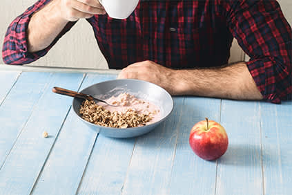 男人吃谷物，咖啡，和一个苹果的健康早餐。