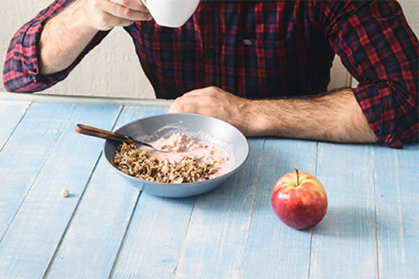 男人吃谷物,咖啡,和一个苹果的健康早餐。
