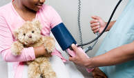 医生为抱着泰迪熊的小女孩检查血压。