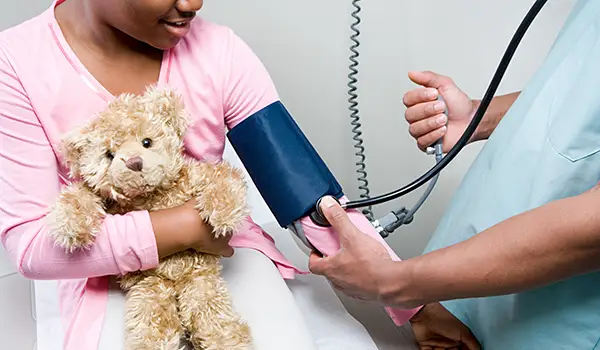 医生给抱着泰迪熊的小女孩测血压。