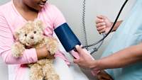 Doctor checking blood pressure of young girl holding teddy bear.