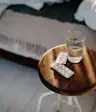White pills and a glass of water on a nightstand next to a bed