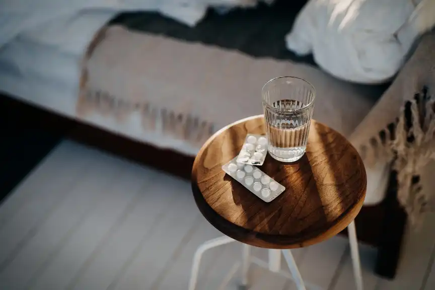 床边的床头柜上放着白色药片和一杯水