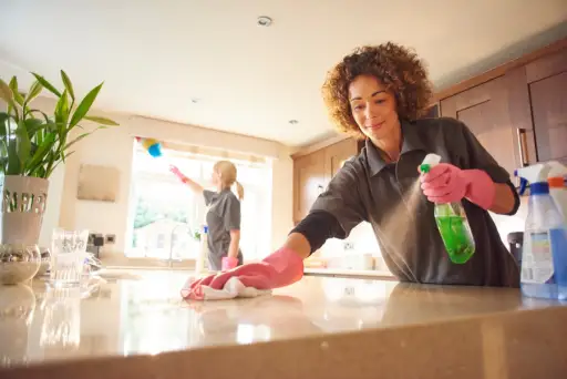 两个专业的清洁工在一个家庭厨房向花岗岩工作表面喷洒清洁剂