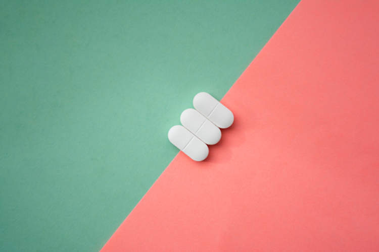 三个白色药丸在绿色和粉红色的分裂背景