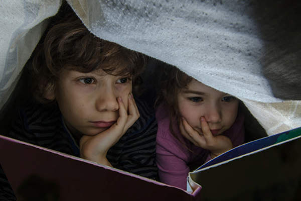 孩子们在毯子下阅读。
